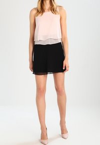 Tvådelat outfit med en ljusrosa ärmlös topp med ett lagerdesign över en svart minikjol, parat med ljusrosa högklackade skor.