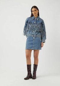 Farkkutakki hapsukoristeilla ja nappikiinnityksellä, yhdistetty istuvaan farkkuhameeseen. Polven korkeuteen ulottuvat ruskeat saappaat täydentävät asun.