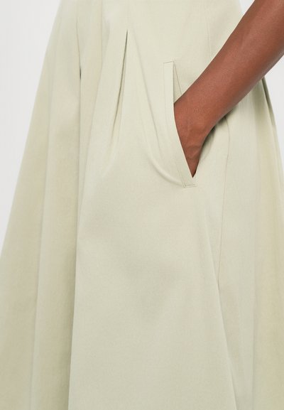 Light green dress with pleats. Features a side pocket and smooth, textured fabric for a structured look. Simple, minimalist design.