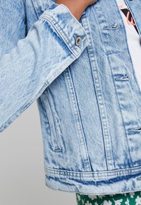 Lichtblauwe denim jas met een vervaagde textuur, voorzien van een kraag, knoopmanchetten en zichtbare stikseldetails.