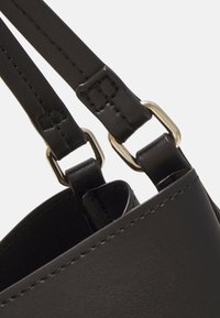 Black leather handbag with adjustable straps. Contains metallic hardware for strap attachment. Smooth texture, minimalistic design.