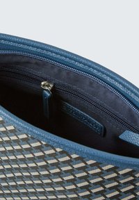 Interno di una borsa blu con motivo, dotato di tasca con zip, caratterizzato da un design geometrico in tonalità di blu scure e chiare, e rifiniture in pelle testurizzata.