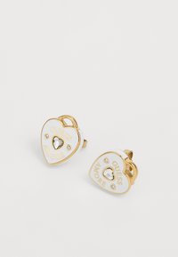 Auksinės širdies formos auskarai su balta emale, kuriuose pateikti žodžiai "GUESS AMORE" ir centrinis skaidrus rhinestone, akcentuoti mažesniais brangakmeniais.