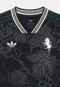 Svart sporttröja med vinranka-mönster, grönrandig krage och silverfärgad Adidas-logga. Har en V-ringning och texturerad tyg.