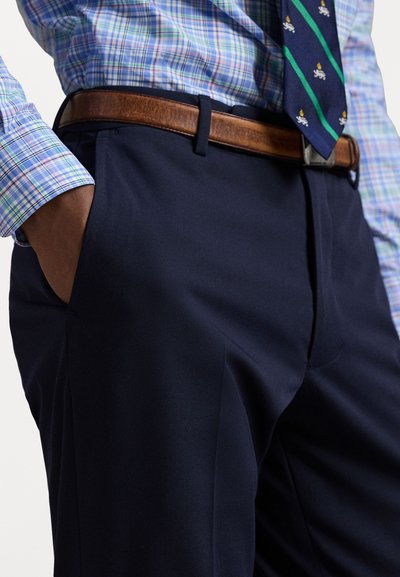 Pantaloni blu navy con una texture liscia abbinati a una camicia a check blu chiaro, verde e bianco con polsini a contrasto e una cravatta a fantasia.