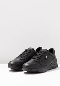Scarpe sportive nere in pelle con una texture liscia, dotate di un design con lacci, suole in gomma e dettagli minimi.
