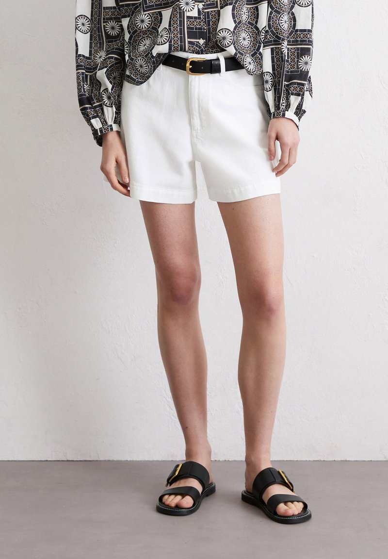 Witte denim shorts met een normale pasvorm, gecombineerd met een zwart-wit gestreept langemouwen shirt en zwarte sandalen met een gouden accent.