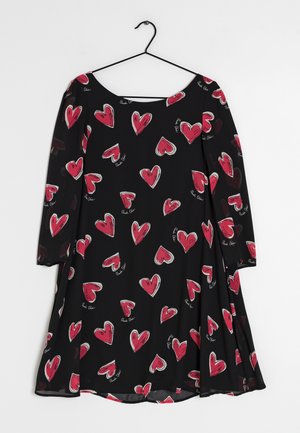 Czarna sukienka z długim rękawem, ozdobiona czerwonymi i białymi wzorami serc oraz drobnymi białymi napisami, wisząca na czarnym drucianym wieszaku na białym tle.