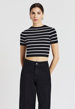 Top corto a righe bianche e nere realizzato in tessuto a costine con maniche corte, abbinato a jeans neri a vita alta con chiusura a bottone.