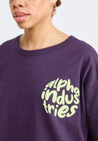 Μωβ βαμβακερό μπλουζάκι με στρογγυλή, ανοιχτό πράσινο λογότυπο "alpha industries" στο στήθος. Διαθέτει στρογγυλή λαιμόκοψη και άνετη εφαρμογή.