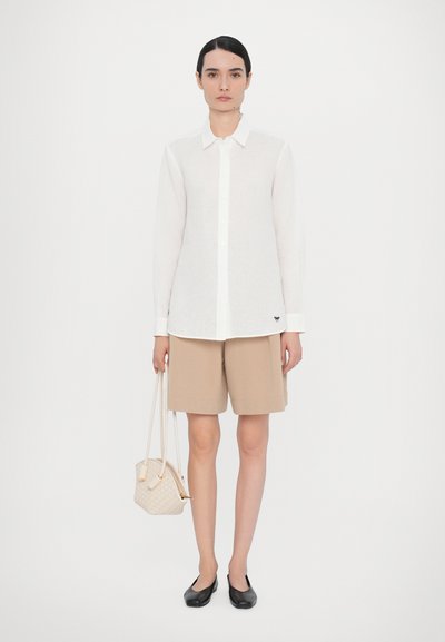 White button-up shirt with long sleeves, paired with beige shorts and black flats. The outfit includes a small woven handbag.