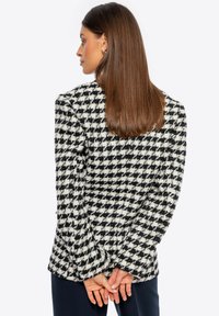 Chaqueta de patrón de pata de gallo en blanco y negro con tejido texturizado, mangas largas y un ajuste estructurado, mostrada desde atrás.