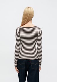 Hosszú ujjú csíkos felső barna és krémszínben, keskeny vízszintes csíkokkal, kerek nyakkivágással, bordázott textúrával, sötét farmernadrággal párosítva.