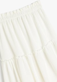Witte gelaagde rok van textuurstof met een gerimpelde tailleband. Kenmerkt rimpelaccenten langs de naadlijnen.