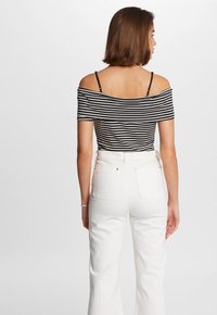 Top de rayas blanco y negro sin mangas combinado con jeans blancos de cintura alta, con bolsillos traseros y un diseño de pierna recta.