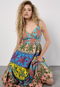 Robe imprimée colorée avec un décolleté en V. Le design présente des sections bleues, roses, jaunes et vertes avec des motifs floraux et des accents.