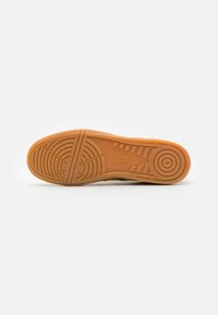 Semelle de chaussure avec une finition en caoutchouc texturé orange. Présente des rainures profondes pour l'adhérence, le logo de la marque "asics" et une forme épurée.