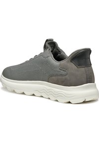 Scarpa sportiva grigia con tomaia in rete, dettagli in suede e una spessa suola bianca. Presenta motivi testurizzati e un logo sul tallone.