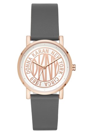Rund urskive med rosaguldfarvet urkasse og gråt læderrem, med en hvid urskive med hævet tekst "DKNY Donna Karan New York Circa 1989".