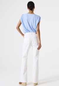 Jeans blancos acampanados con cintura alta y dos bolsillos en la parte posterior, acompañados de una blusa de manga corta de color azul claro con un corte relajado y tejido texturizado.