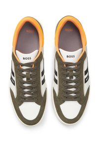 Weiße Ledersneaker mit grünen Veloursakzenten, schwarzen Streifen und orangefarbenem Innenfutter. Verfügen über braune Schnürsenkel und "BOSS"-Logo auf der Zunge.