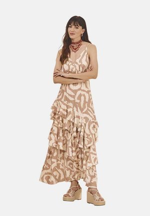 Vestido maxi en beige claro con patrón abstracto en crema, con tirantes finos y una silueta fluida. Combinado con sandalias de cuña.