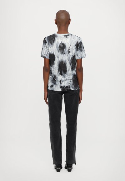 Melnā un pelēkā krāsu t-krekls ar saisti, ar apaļu kakla līniju, kuram ir abstrakts raksts; apvienots ar melniem džinsiem un augstpapēžu kurpēm.