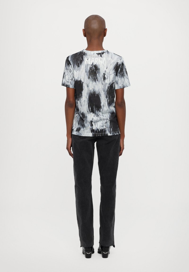 T-shirt tie-dye noir et gris avec un col rond, présentant un motif abstrait ; associé à un jean noir et des chaussures à talons.