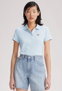 Polo-shirt bleu clair avec un col, arborant un logo rouge Levi's. Associé à un short en denim clair taille haute au coupes classique.