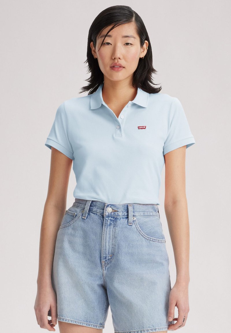 Polo-shirt bleu clair avec un col, arborant un logo rouge Levi's. Associé à un short en denim clair taille haute au coupes classique.