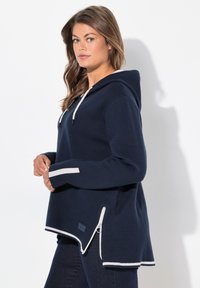 Marineblauer Hoodie mit weißen Akzenten, langen Ärmeln, seitlichem Reißverschlussdetail und lässiger Passform. Hergestellt aus weichem Stoff, mit einer Kapuze und gerippten Bündchen.