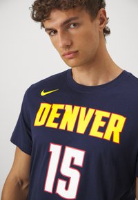 Tumši zils Nike T-krekls ar izteiksmīgu dzeltenu "DENVER" tekstu un baltu "15" priekšpusē, ar apaļu kakla izgriezumu un īsām piedurknēm.
