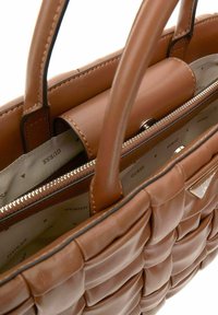 Sac à main en cuir marron avec un design matelassé, deux poignées et une poche zippée à l'intérieur avec un doublure à logo. Accents en matériel argenté.