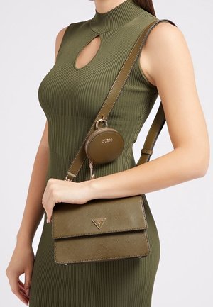 Femme portant une robe olive sans manches en maille côtelée, avec un sac bandoulière olive assorti et une petite pochette ronde pour pièces arborant les logos GUESS.