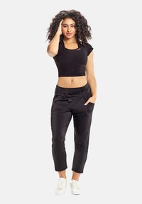 Sort cropped top med korte ærmer, parret med løstsiddende sorte bukser med lommer og en glat tekstur; båret med hvide sneakers.