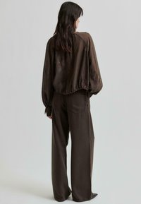 Blouse marron surdimensionnée avec broderies florales, ourlet cintré ; associée à un pantalon large taille haute marron, créant une silhouette décontractée.