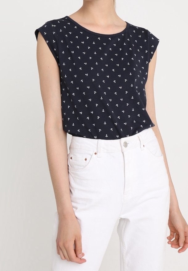 Námořnická modrá bezramínková halenka s malými bílými vzory kotvy, spárovaná s bílými džínami se zvýšeným pasem, na stojící osobě.