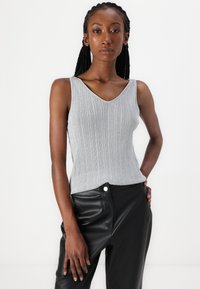 Grijze geribbelde tanktop met een V-hals, gemaakt van rekbare stof, gecombineerd met high-waisted zwarte faux leren broeken.