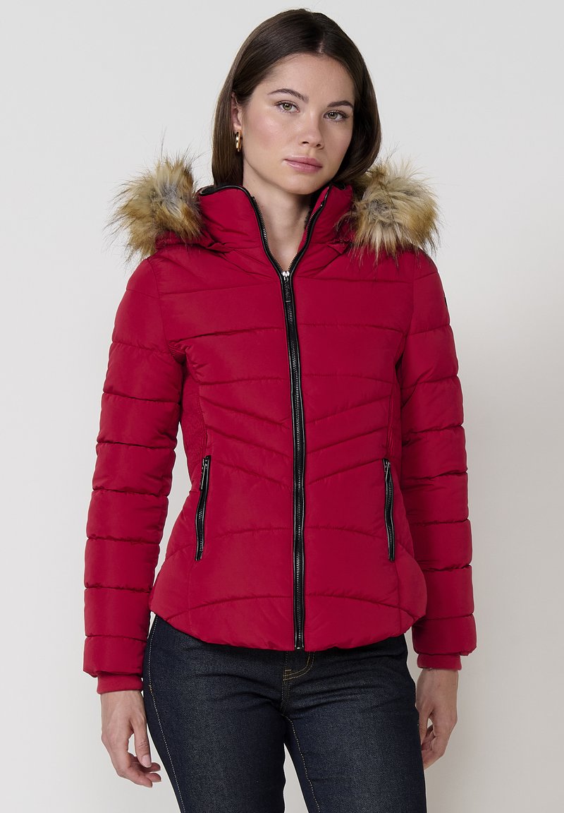 Raudonas pūkinis švarkas su horizontaliai siūtais raštais, juoda užtrauktuką ir kailiniu apvadu ant gobtuvo. Yra dvi užtrauktuku uždaromos šoninės kišenės ir prigludusi siluetas.