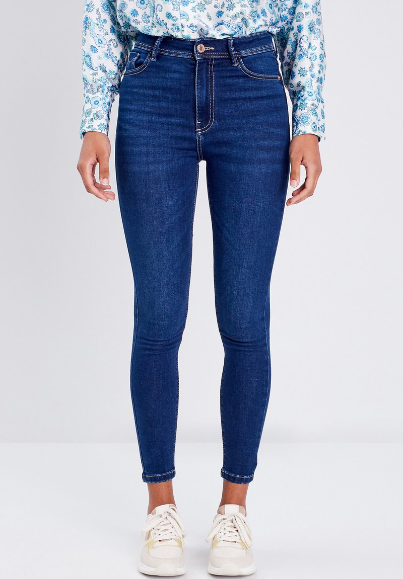 Jeans in denim blu a vita alta con una vestibilità skinny, dotati di cinque tasche, cuciture sottili e chiusura con bottone.