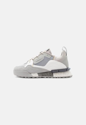 Low-top sneaker in shades of gray and white with mixed materials, a patterned sole, and side branding reading "Replay."