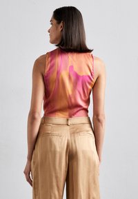 Ermeløs topp i gradient rosa og oransje satin, med en rund halslinning. Kombinert med beige skreddersydde bukser med baklommer.