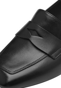 Mocassins en cuir noir avec une texture lisse, bout arrondi et une bande décorative au-dessus avec un design découpé.
