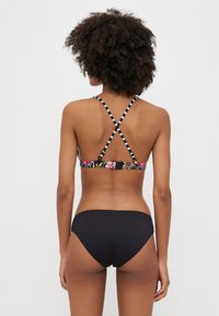 Bikini-set med en blommönstrad topp med justerbara svartvita remmar, kombinerat med enfärgade svarta underdelar. Slät textur.