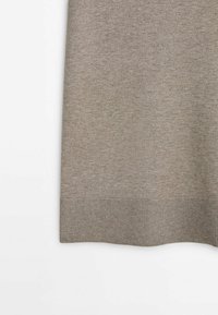 Tissu tricoté marron doux avec un bord côtelé sur un fond clair, montrant la texture et les détails des coutures.