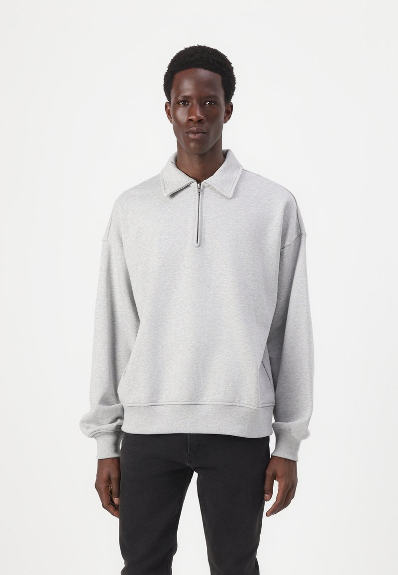 Sweatshirt cinza com colarinho com fecho, corte solto, punhos canelados e cintura elástica. Textura suave e design minimalista.