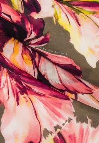 Tessuto floreale con grandi stampe di fiori rosa e gialli su uno sfondo marrone scuro. Il design presenta texture morbide e drappeggi fluidi.