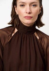 Bruine blouse met hoge hals van doorschijnende stof, met een gathered halslijn en uitsnijdingen op de schouders. Glad textuur.