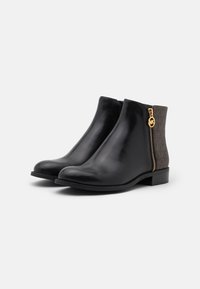 Bottines en cuir noir avec un bout arrondi, dotées d'une fermeture éclair dorée sur le côté et d'un panneau arrière à motif marron. Texture lisse.