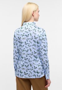 Lichtblauwe blouse met een algehele vlinderprint in groen en wit. Lange mouwen met een knoopsluiting bij de manchetten. Vlotte textuur.